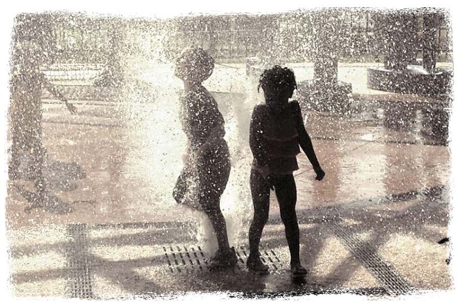 Two children playing in a water fountain
